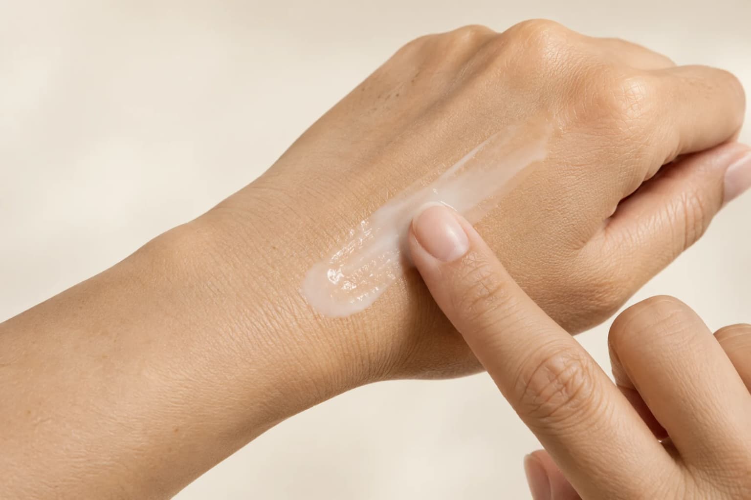 A fingertip spreading a thin milky serum layer on the back of a naturally textured hand. Editorial texture illustration.