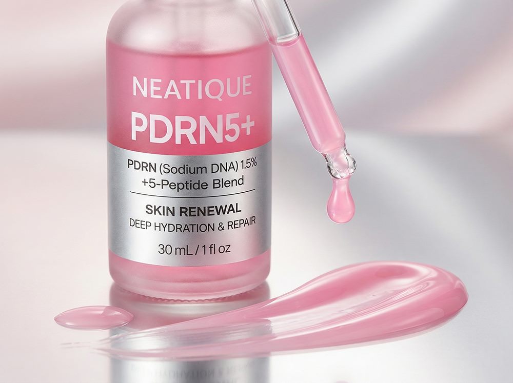 Close-up editorial image of Neatique PDRN Serum highlighting the branded bottle and silky pink serum texture